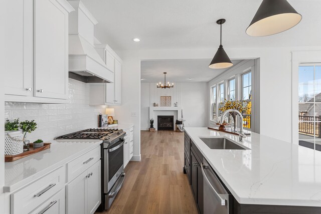 kitchen featuring a sink, backsplash, custom range hood, stainless steel appliances, and a kitchen island with sink