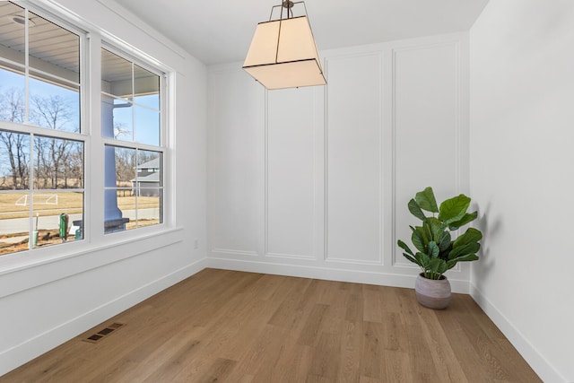 unfurnished dining area featuring a decorative wall, baseboards, visible vents, and light wood finished floors