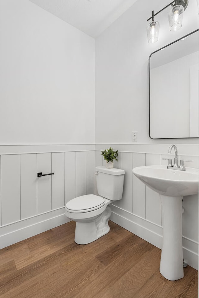 half bath featuring toilet, wood finished floors, a wainscoted wall, and a sink