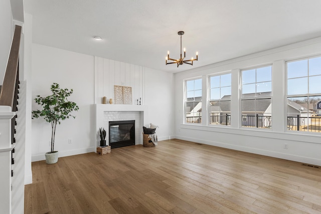 unfurnished living room with wood finished floors, visible vents, baseboards, an inviting chandelier, and a brick fireplace