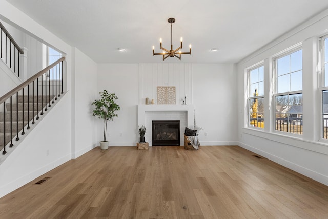 unfurnished living room featuring visible vents, a brick fireplace, stairs, an inviting chandelier, and wood finished floors