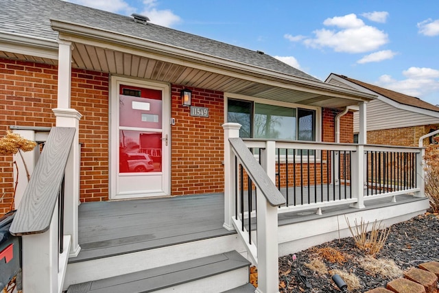 property entrance featuring roof with shingles, a porch, and brick siding