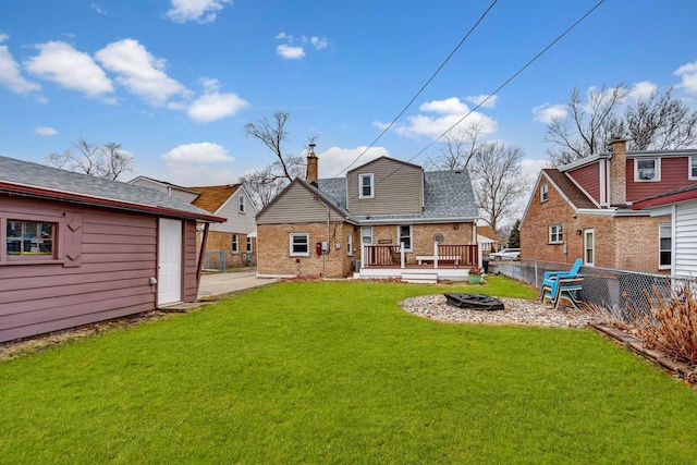 rear view of property with brick siding, a yard, a chimney, an outdoor fire pit, and fence