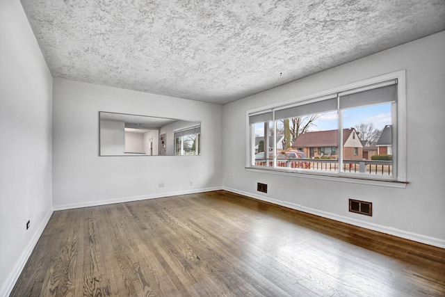 spare room with wood finished floors, visible vents, and baseboards