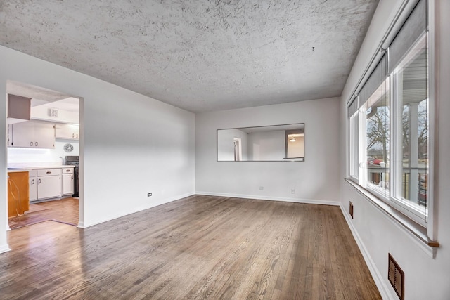 unfurnished room with a textured ceiling, wood finished floors, visible vents, and baseboards