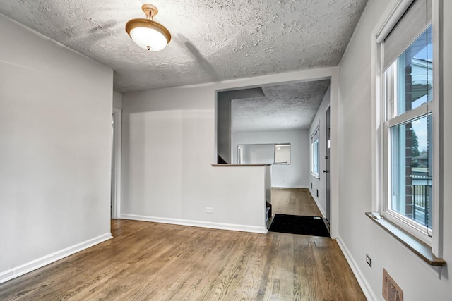 empty room featuring visible vents, a textured ceiling, baseboards, and wood finished floors