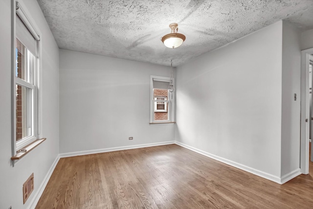 spare room with visible vents, a textured ceiling, baseboards, and wood finished floors