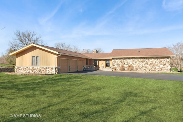 view of front of property featuring driveway, stone siding, a front yard, a garage, and a chimney