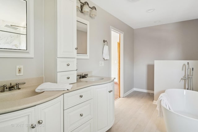 full bathroom with a freestanding bath, double vanity, wood finished floors, and a sink