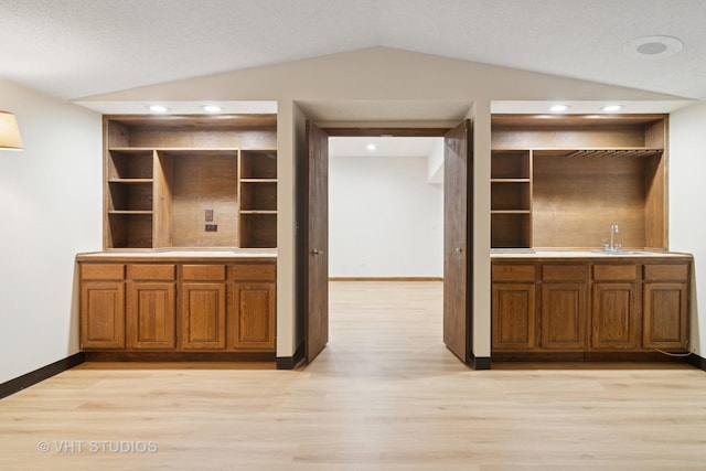 kitchen featuring brown cabinetry, a sink, vaulted ceiling, and open shelves