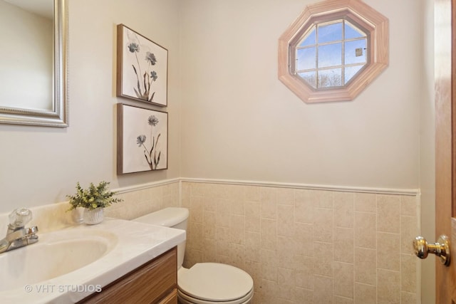 bathroom with tile walls, a wainscoted wall, toilet, and vanity