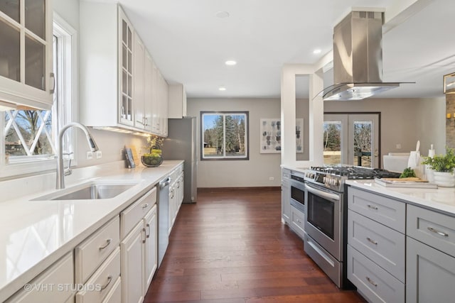 kitchen with island exhaust hood, a sink, dark wood-style floors, stainless steel appliances, and light countertops