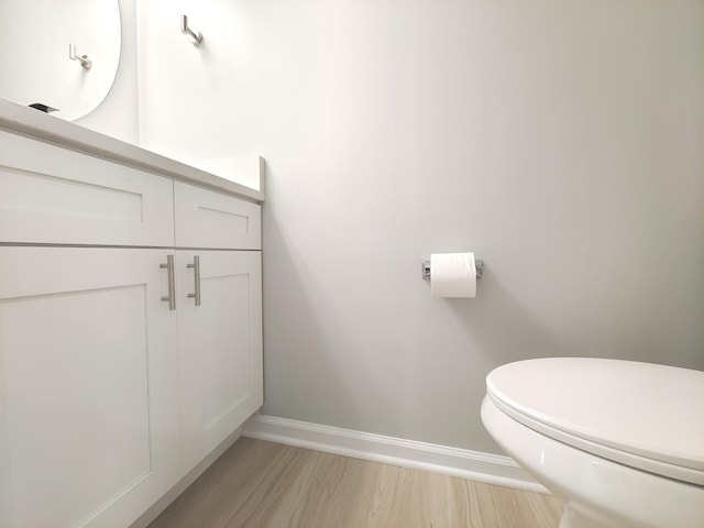 half bath with toilet, vanity, baseboards, and wood finished floors