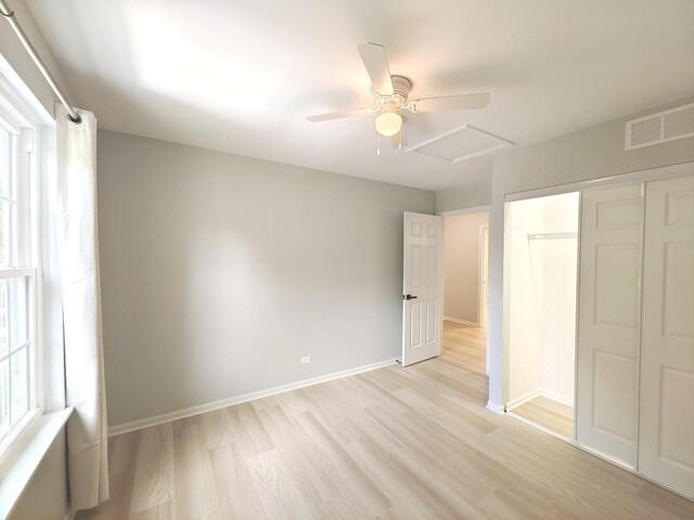unfurnished bedroom featuring a closet, visible vents, attic access, light wood-style floors, and baseboards