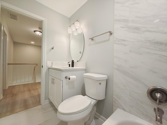 bathroom featuring a washtub, toilet, vanity, baseboards, and marble finish floor