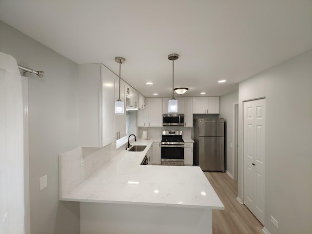 kitchen with a peninsula, a sink, white cabinetry, appliances with stainless steel finishes, and light wood finished floors