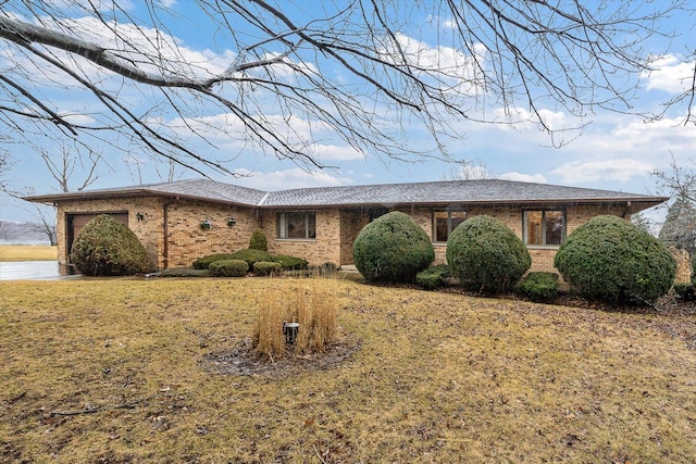 ranch-style home featuring an attached garage, roof with shingles, a front lawn, and brick siding