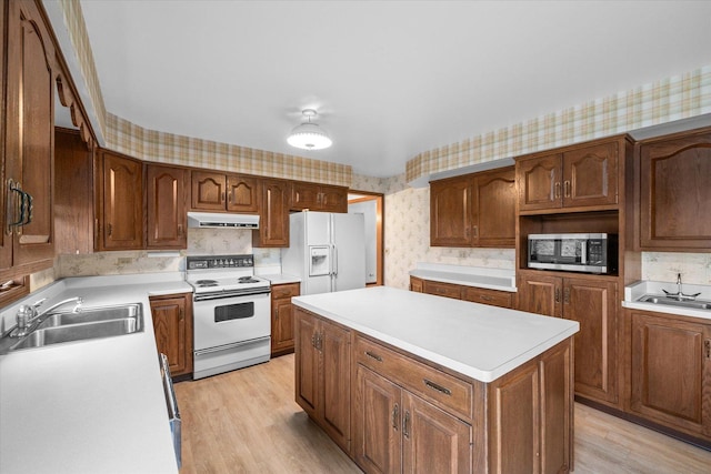 kitchen with wallpapered walls, white appliances, a kitchen island, under cabinet range hood, and a sink