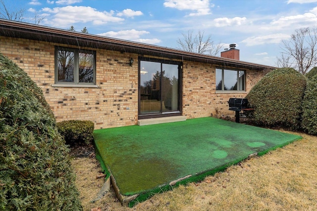 back of house with a chimney, a lawn, and brick siding