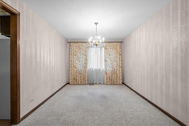 carpeted empty room featuring a chandelier, baseboards, and wallpapered walls