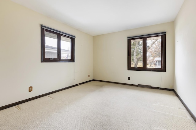 unfurnished room with a healthy amount of sunlight, light colored carpet, and baseboards