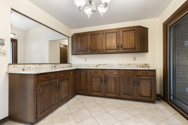 kitchen with dark brown cabinetry, light tile patterned floors, a peninsula, light stone countertops, and an inviting chandelier