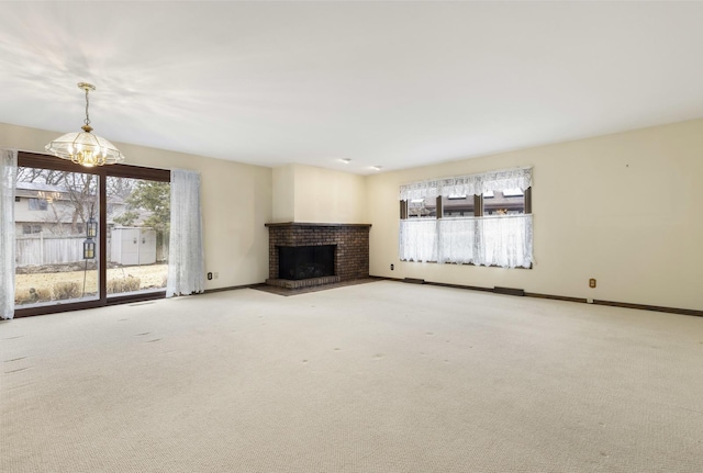 unfurnished living room featuring a brick fireplace, carpet flooring, a notable chandelier, and baseboards