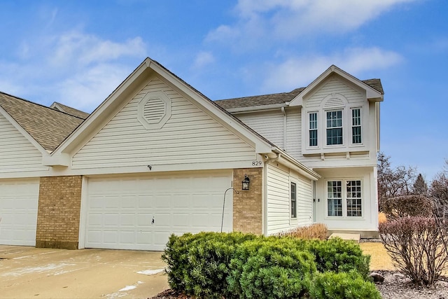 traditional home featuring concrete driveway, brick siding, an attached garage, and a shingled roof