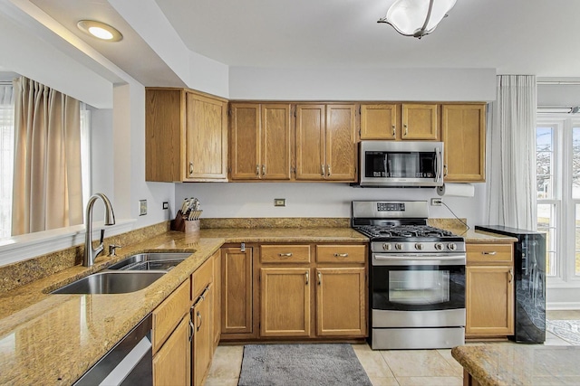 kitchen with stainless steel appliances, a wealth of natural light, a sink, and light stone counters