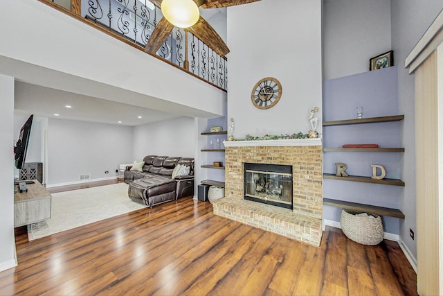 living area with visible vents, a towering ceiling, a brick fireplace, wood finished floors, and baseboards