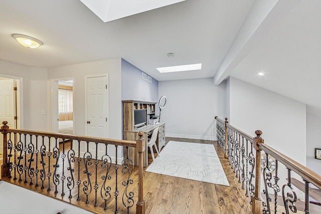 hall with vaulted ceiling with skylight, wood finished floors, visible vents, an upstairs landing, and baseboards