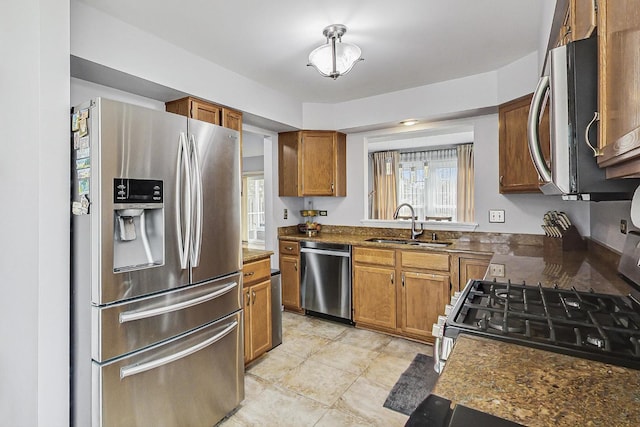 kitchen featuring appliances with stainless steel finishes, brown cabinetry, dark countertops, and a sink