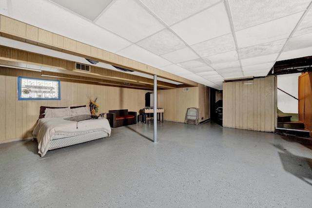 bedroom with speckled floor, a drop ceiling, visible vents, and wooden walls