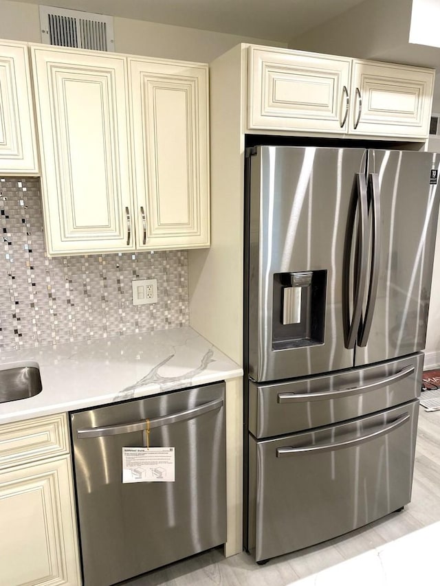 kitchen featuring backsplash, visible vents, stainless steel appliances, and cream cabinetry