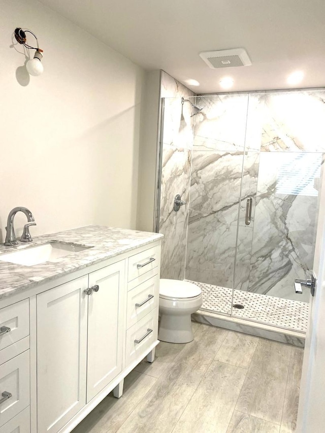 bathroom with toilet, a marble finish shower, wood finished floors, and vanity