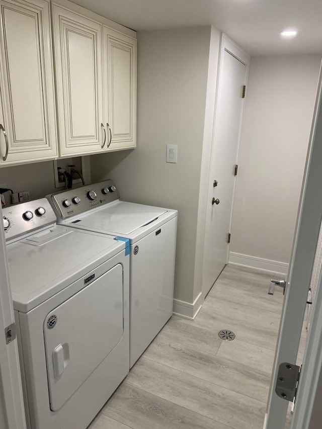 laundry room with light wood-type flooring, cabinet space, baseboards, and washer and clothes dryer