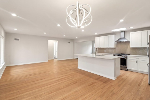 kitchen featuring visible vents, light wood-style floors, stainless steel gas stove, wall chimney exhaust hood, and a sink