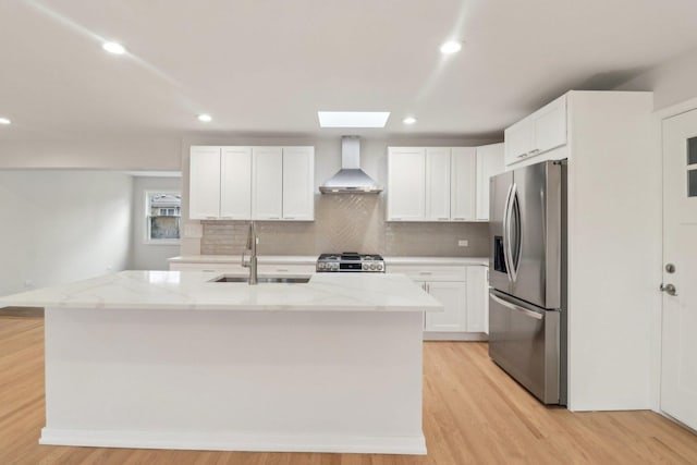 kitchen featuring light stone countertops, stainless steel fridge with ice dispenser, a sink, stove, and wall chimney range hood