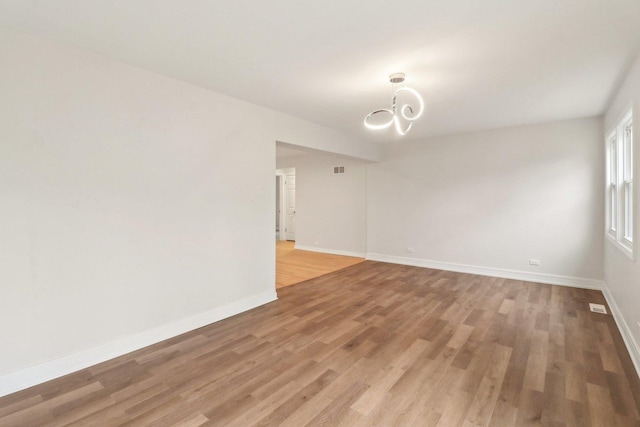 unfurnished room featuring visible vents, baseboards, light wood finished floors, and a chandelier