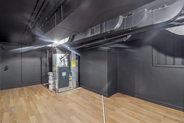 unfinished basement featuring visible vents, heating unit, and wood finished floors