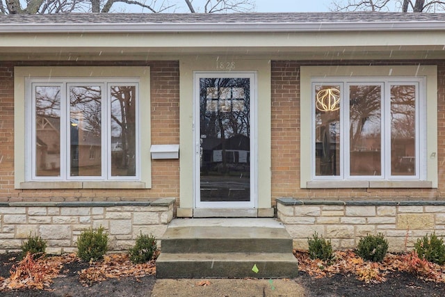 entrance to property with brick siding, stone siding, and roof with shingles