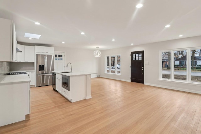 kitchen featuring light wood-type flooring, a sink, white cabinetry, appliances with stainless steel finishes, and light countertops