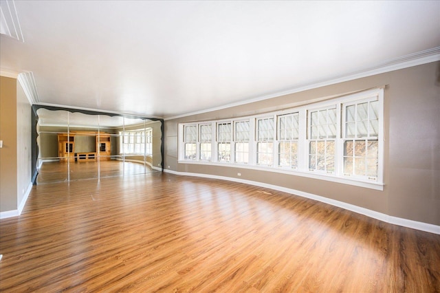 unfurnished living room featuring baseboards, crown molding, and wood finished floors