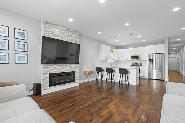 living room featuring recessed lighting, baseboards, a stone fireplace, and dark wood-style flooring