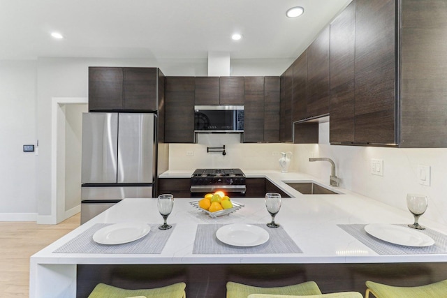 kitchen with appliances with stainless steel finishes, a kitchen bar, a sink, and dark brown cabinetry