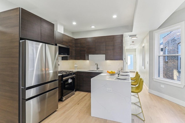 kitchen with stainless steel appliances, a breakfast bar area, a sink, and light wood finished floors