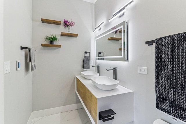 full bath featuring marble finish floor, a sink, baseboards, and double vanity