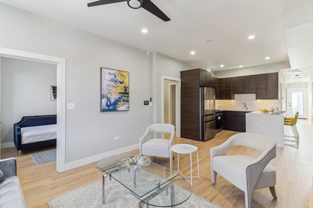 living room featuring baseboards, light wood-type flooring, a ceiling fan, and recessed lighting