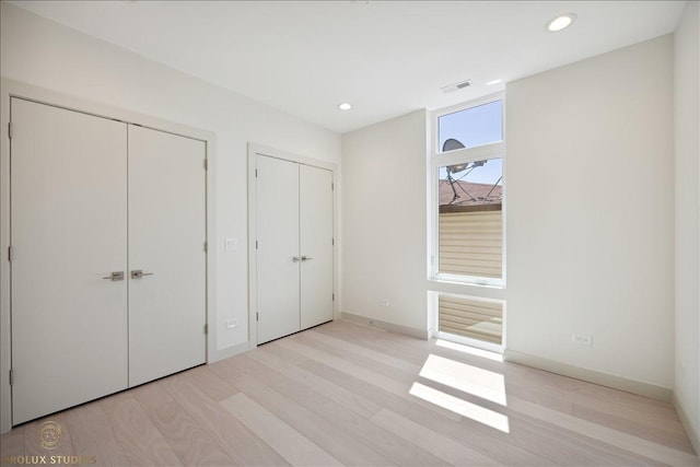 unfurnished bedroom featuring baseboards, recessed lighting, two closets, and light wood-style floors