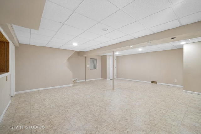 finished basement with a paneled ceiling, baseboards, and tile patterned floors